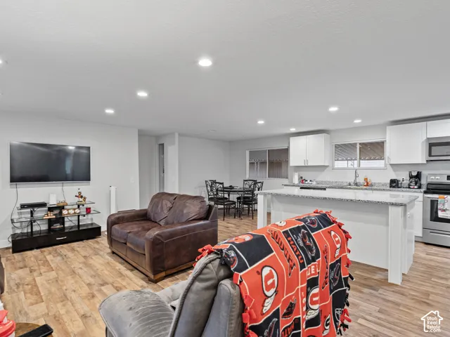 Open-concept interior featuring wood-finish flooring, recessed lighting, white cabinetry, a kitchen island with stone-finish countertops, and stainless steel appliances