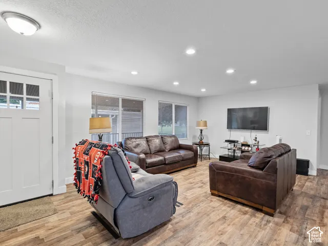 Open-concept interior featuring wood-finish flooring, recessed lighting, and a white six-panel exterior door with glass detailing
