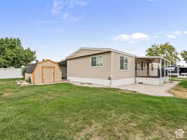 Exterior featuring tan horizontal siding, a covered porch with metal railing, a detached storage shed, and a gravel and grass yard
