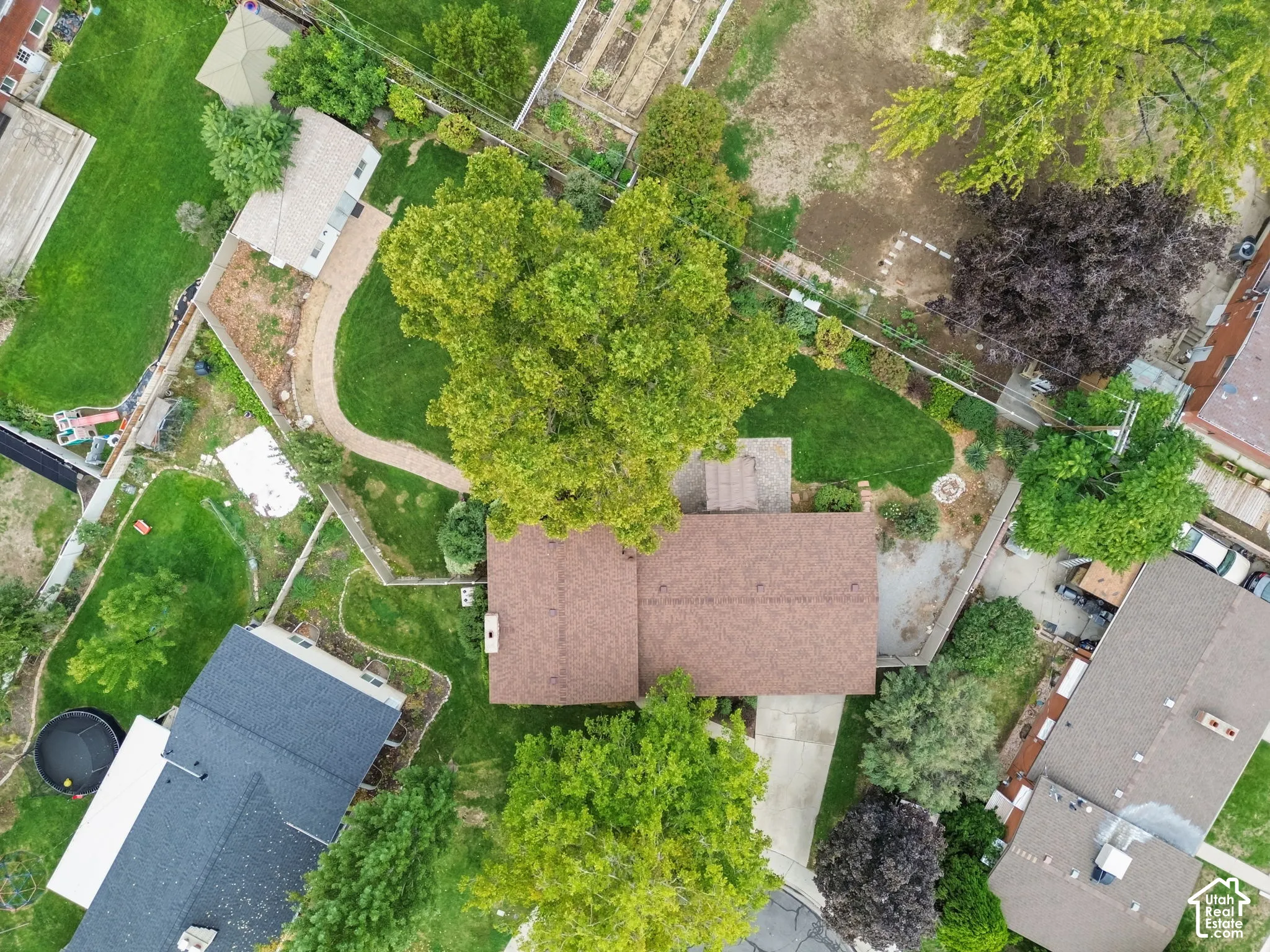 Aerial perspective featuring a spacious lot with mature trees, expansive lawn area, paved walkway, and a concrete driveway