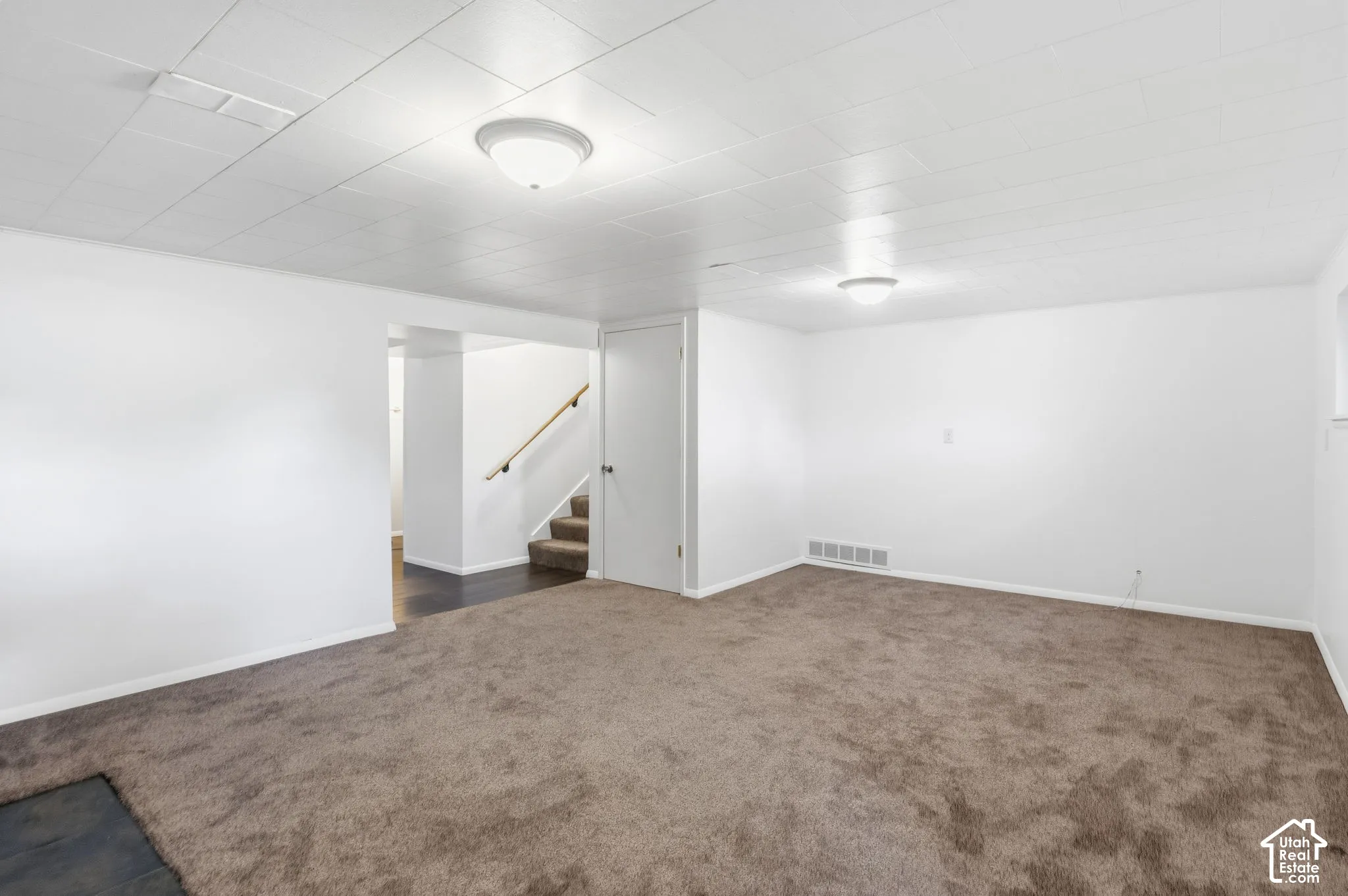 Stairs leading to basement 2 level. Neutral-toned carpeted flooring, white panel ceiling, flush-mount lighting, and solid-core interior door