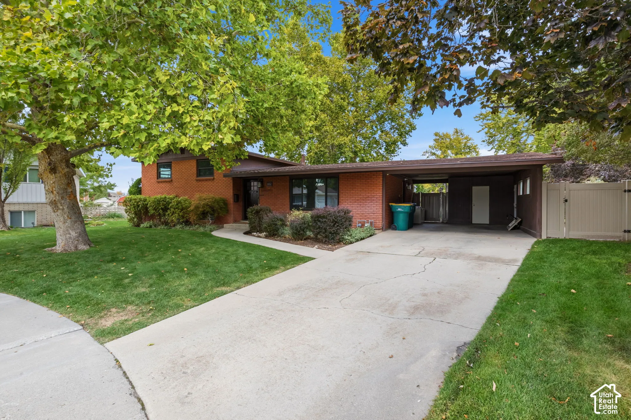 Single-story residence featuring a red brick exterior, concrete driveway, attached carport, and mature landscaping