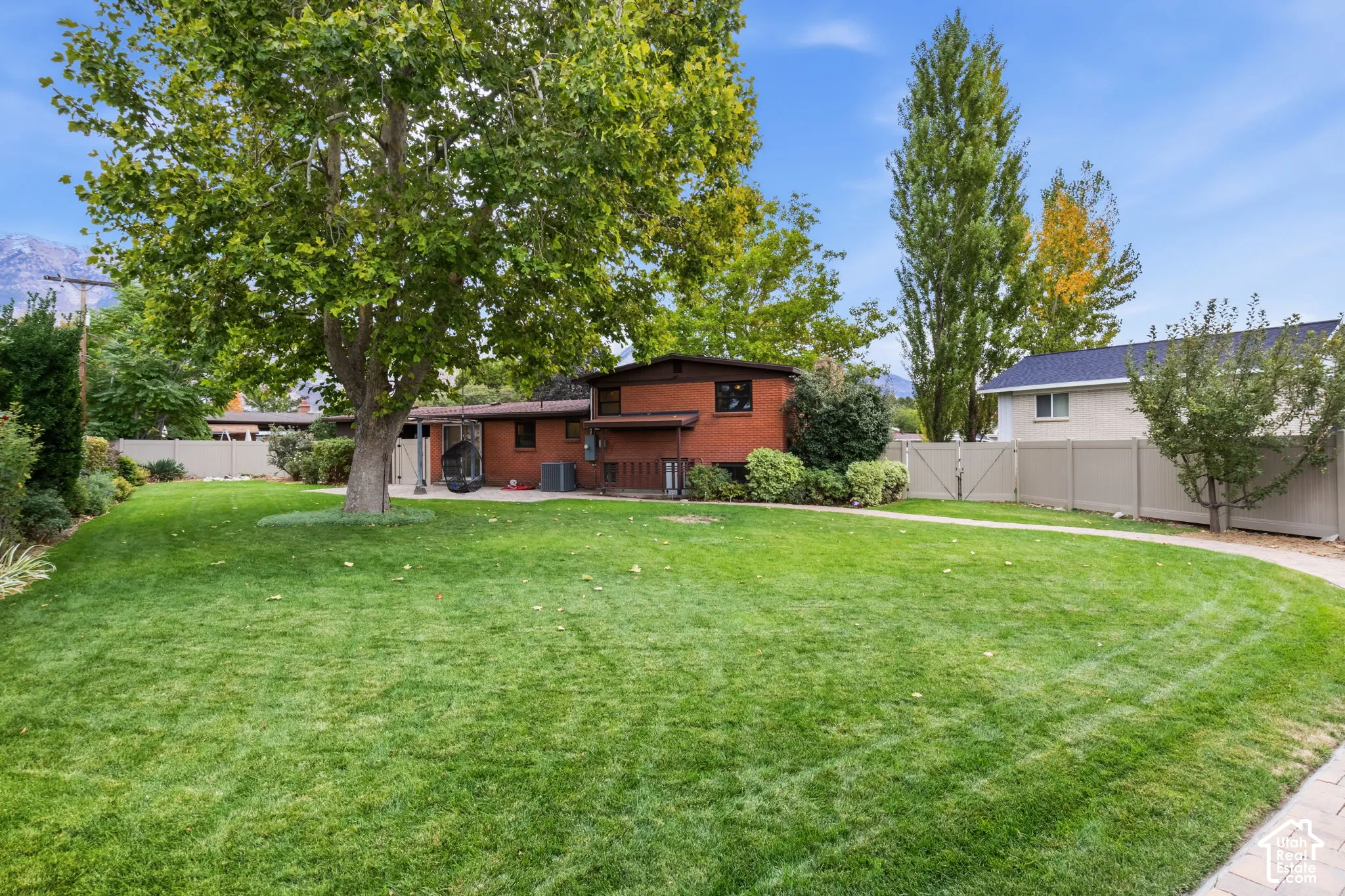 Expansive backyard featuring a brick exterior, mature trees, manicured lawn, and perimeter privacy fencing