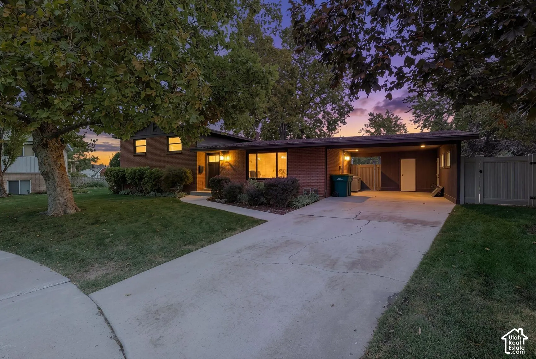 Brick exterior residence featuring a concrete driveway, attached carport, and mature trees