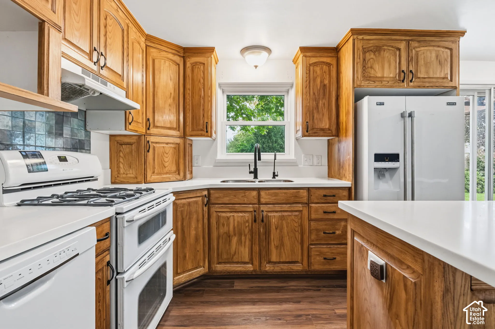 Kitchen featuring wood cabinetry, solid-surface countertops, wood-finish flooring, dual-basin sink with a matte black faucet, and a tile backsplash