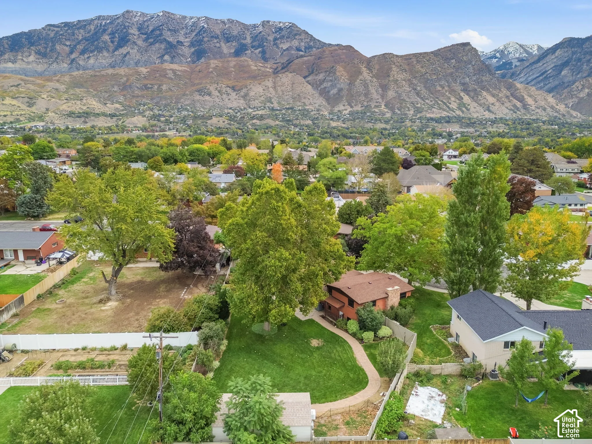 Aerial perspective featuring a landscape with mature deciduous trees, a winding stone path, expansive grass lawn, and a prominent mountain range backdrop