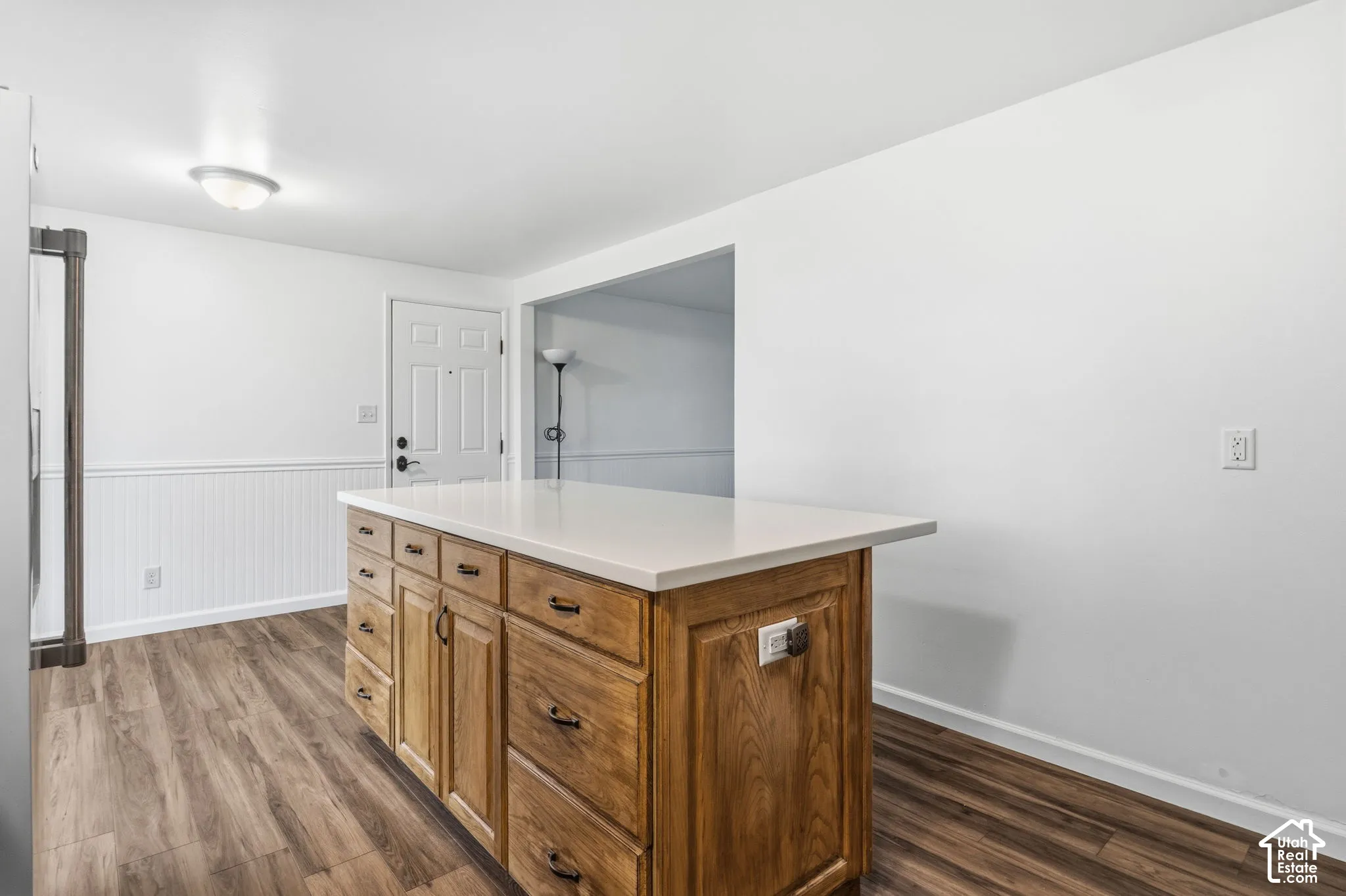 Kitchen island featuring wood cabinetry and a solid-surface countertop, complemented by wood-finish flooring and white beadboard wainscoting
