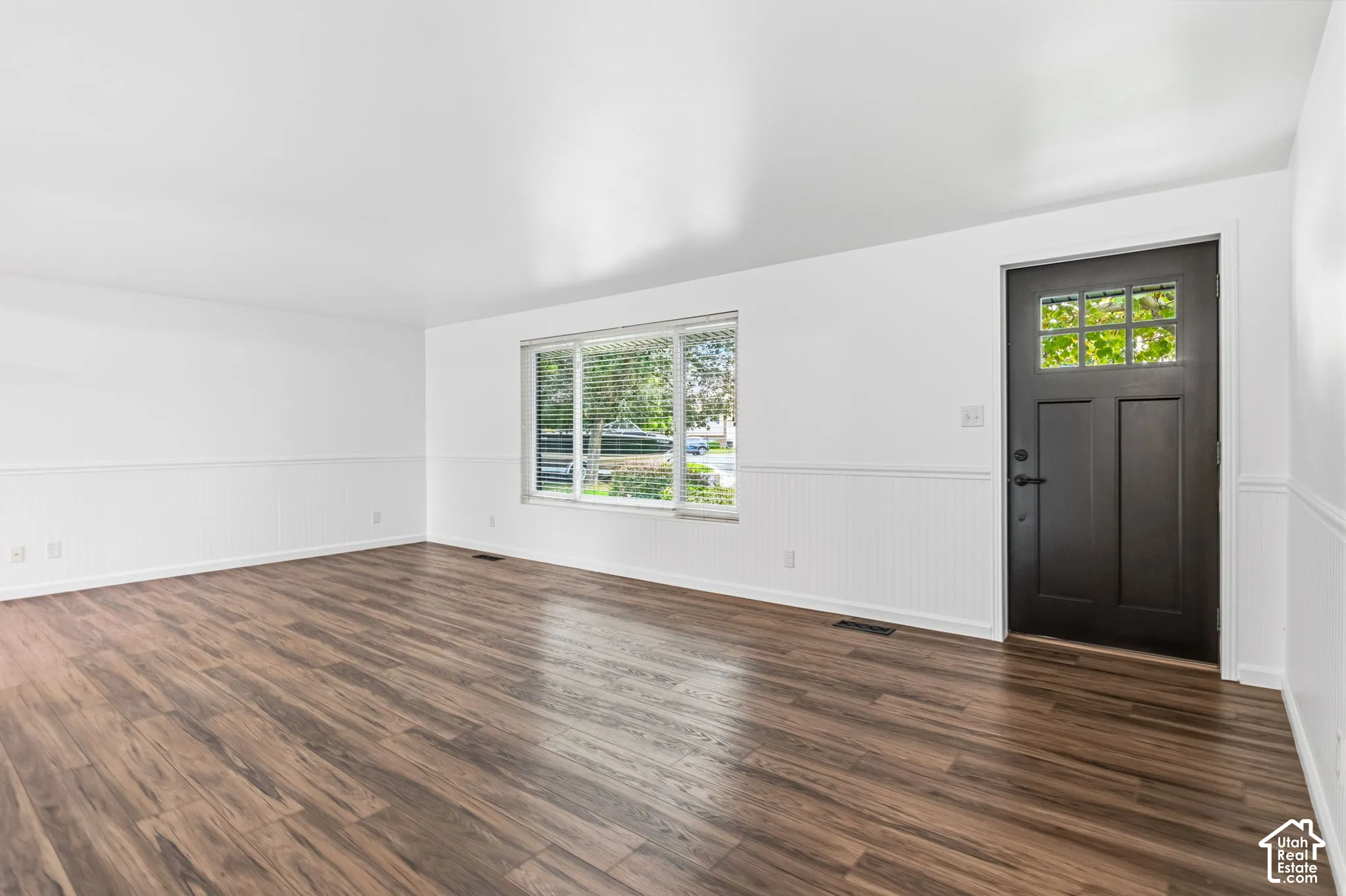 Entry and living room-Interior space featuring wood-finish flooring, white beadboard wainscoting, a multi-pane window, and a dark-toned entry door with a glass inlay