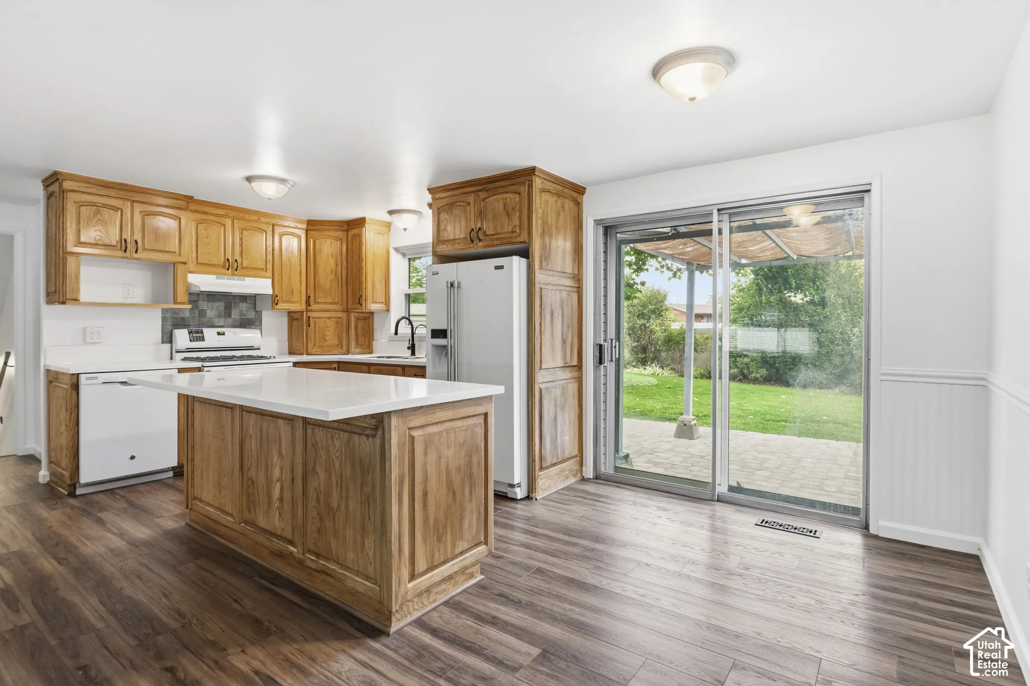 Kitchen featuring wood cabinetry, a central island with a solid-surface countertop, wood-finish flooring, and sliding glass doors with access to a paved outdoor area