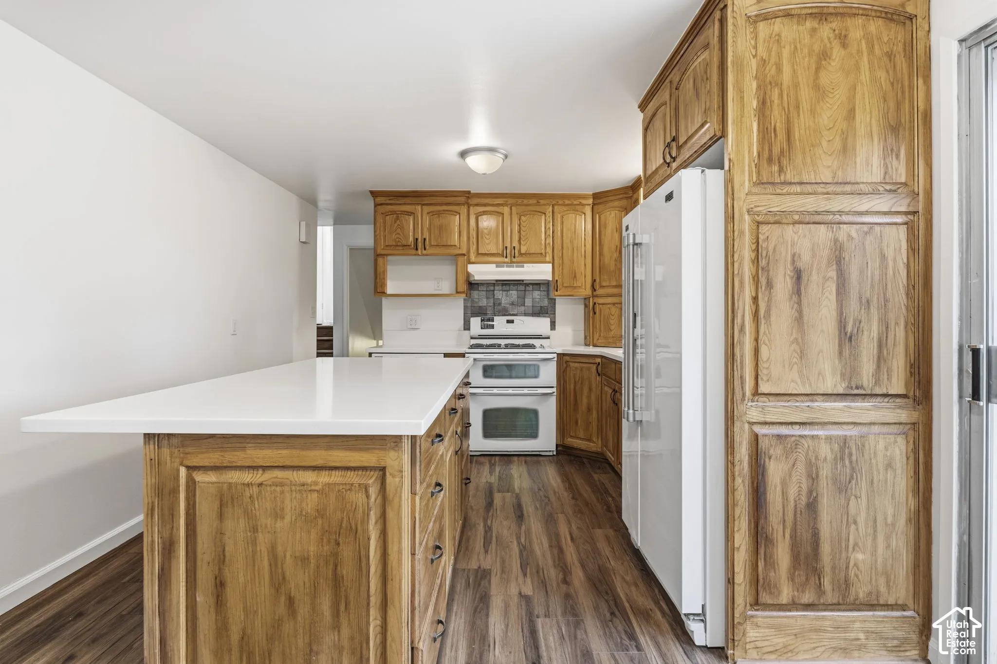 Kitchen featuring wood cabinetry, quartz-topped island, white appliances, tiled backsplash, and wood-finish flooring