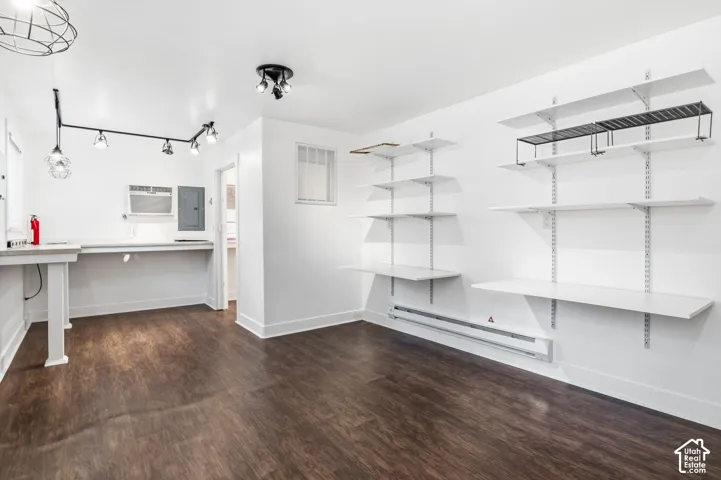 Wood-finish flooring, wall-mounted adjustable shelving, multi-head track lighting, and a built-in counter surface