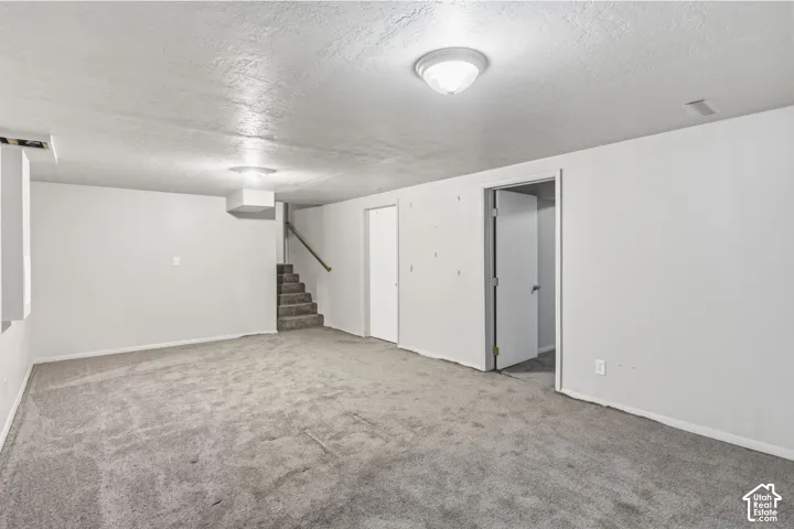 Stairs leading to basement 2-Neutral-toned interior space featuring wall-to-wall carpeting, white walls, flush-mount lighting, and an enclosed staircase with a handrail