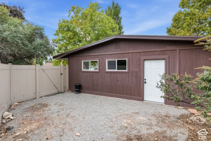 Detached structure featuring wood-panel siding, dual sliding windows, an exterior entry door, and a gravel yard area enclosed by vinyl privacy fencing