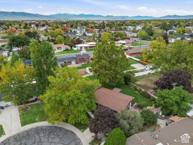 Aerial perspective of a residential property featuring a cul-de-sac location, mature tree canopy, grass lawn, and mountainous horizon