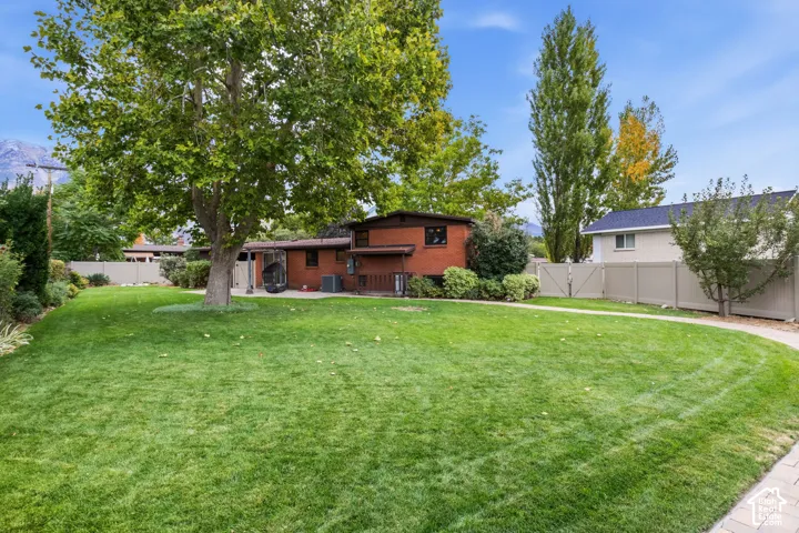 Expansive backyard featuring a brick exterior, mature trees, manicured lawn, and perimeter privacy fencing