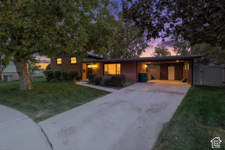 Brick exterior residence featuring a concrete driveway, attached carport, and mature trees