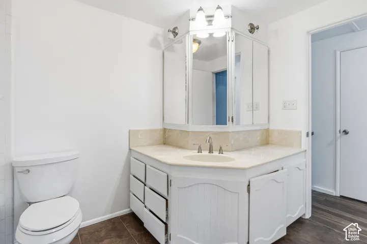 Corner vanity featuring white cabinetry, integrated stone-finish countertop, undermount sink with centerset faucet, and multi-panel mirrored medicine cabinet