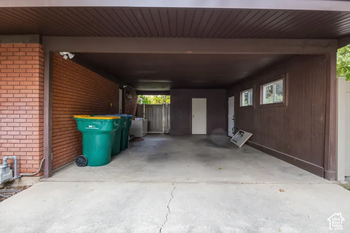 Covered carport featuring a concrete floor, red brick exterior wall, dark wood-finish siding, and two exterior access doors