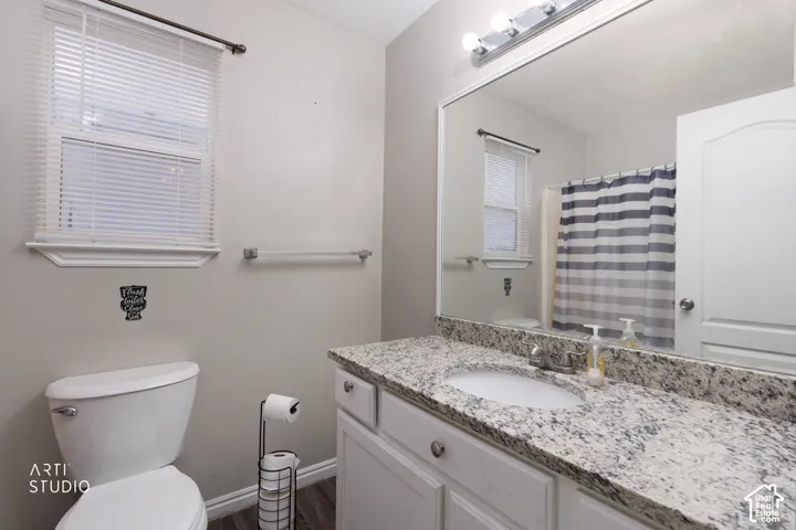 Vanity featuring a stone countertop with an integrated basin, white cabinetry, a full-width wall mirror, and an overhead vanity light fixture