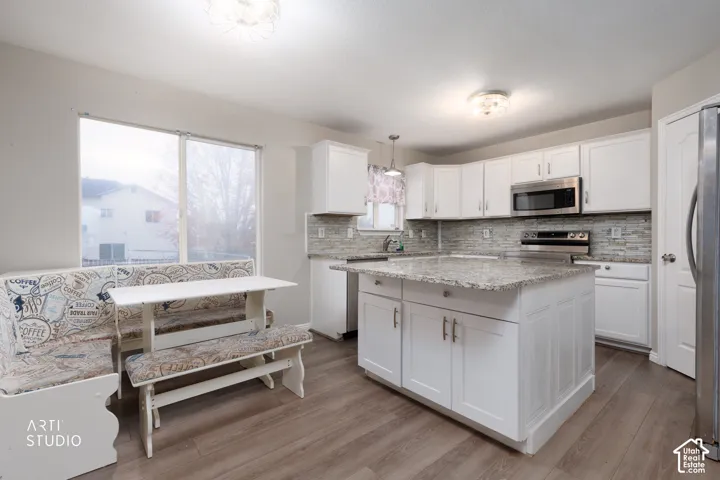 Kitchen featuring white cabinetry, stone-surface countertops, central island, tiled backsplash, and wood-finish flooring