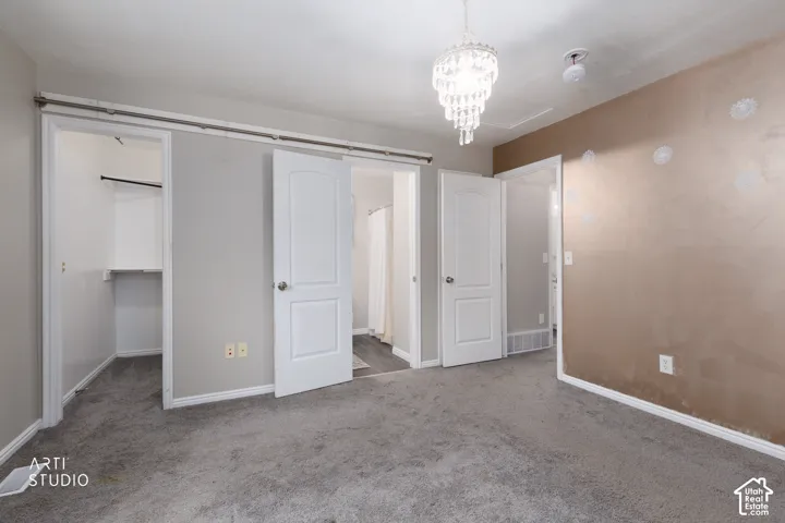 Room featuring wall-to-wall carpeting, a crystal-style drop chandelier, three solid-core panel doors, and a walk-in closet with built-in shelving