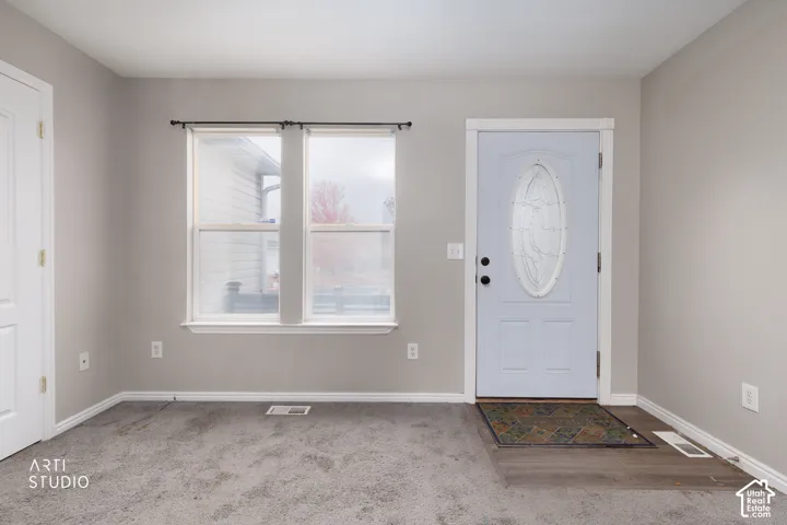 Entryway featuring a light blue front door with an oval glass insert, neutral-toned wall paint, dual windows, and multi-textural flooring consisting of carpet and wood-finish planks