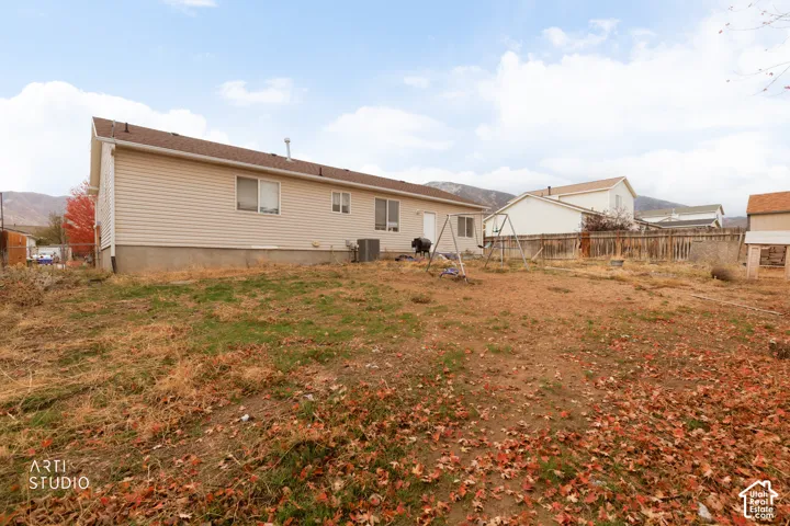 Exterior featuring vinyl siding, asphalt shingle roofing, and a fenced-in lot with mountain surroundings