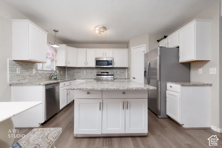 Kitchen featuring white shaker-style cabinetry, stone-finish countertops, a central island, stainless steel appliances, and a linear tile backsplash
