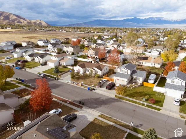 Aerial perspective showcasing a residential neighborhood featuring mountain topography, mature foliage, and paved street access