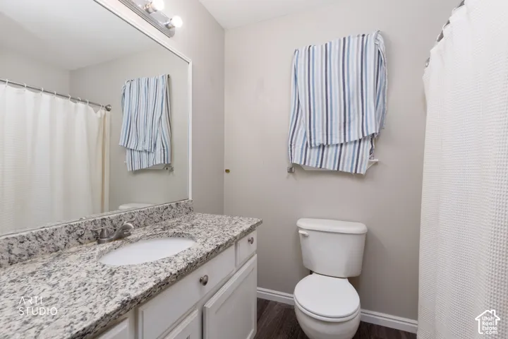 Bathroom featuring a stone-patterned countertop with an integrated basin, white cabinetry, a large wall-mounted mirror, and wood-finish flooring