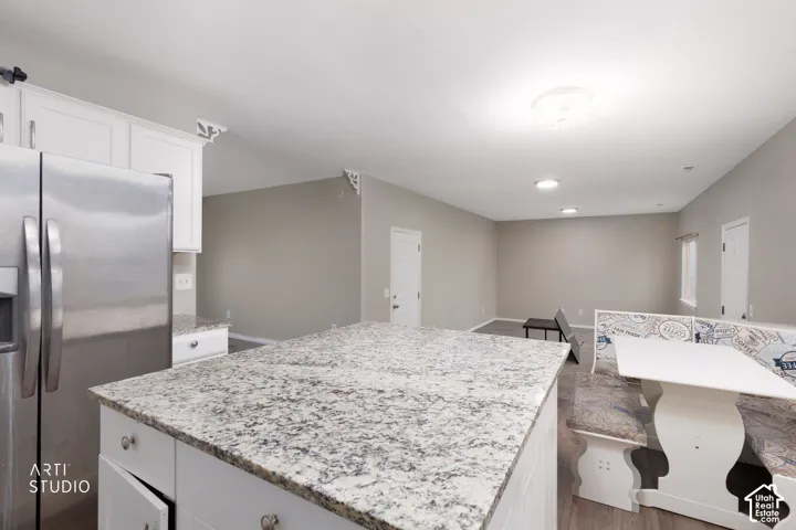 Kitchen featuring white shaker-style cabinetry, stone-surface island countertop, stainless steel refrigerator, and wood-finish flooring