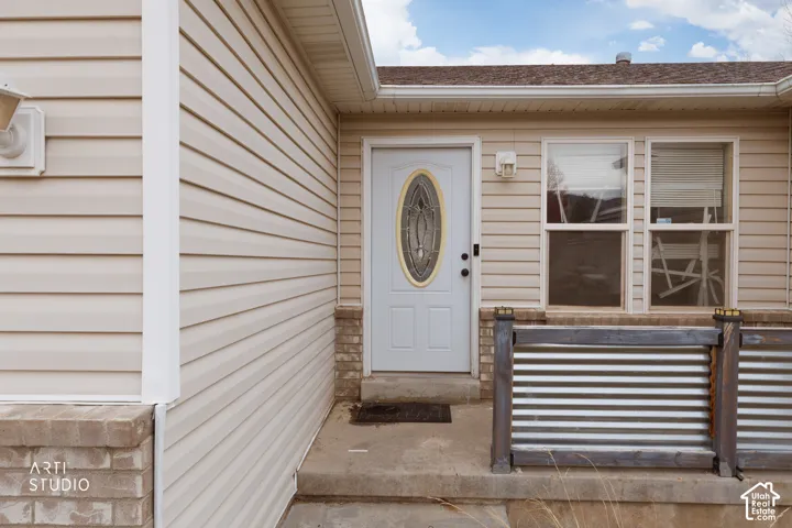 Exterior entrance featuring beige horizontal siding, stone veneer accents, a single-lite entry door with an oval glass insert, and a corrugated metal porch railing
