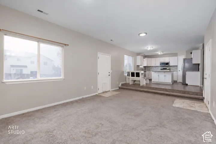Open-concept interior featuring wall-to-wall carpeting, raised kitchen platform with wood-finish flooring, white cabinetry, integrated kitchen island, and recessed lighting