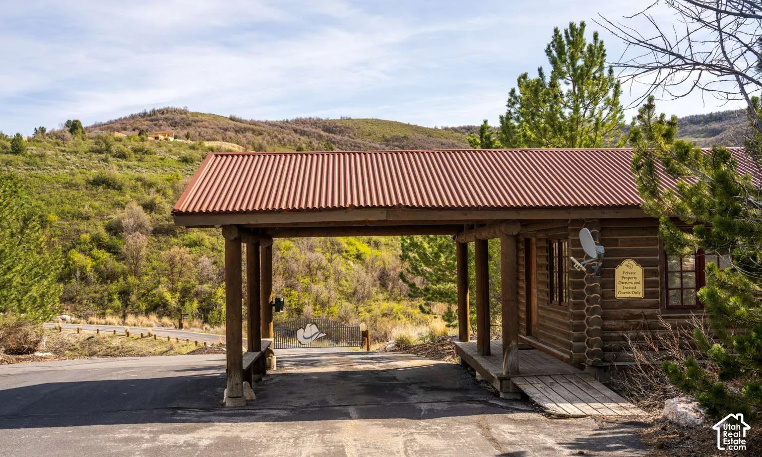 Rustic log cabin structure featuring a corrugated metal roof, covered entryway with wooden support posts, and natural timber exterior walls