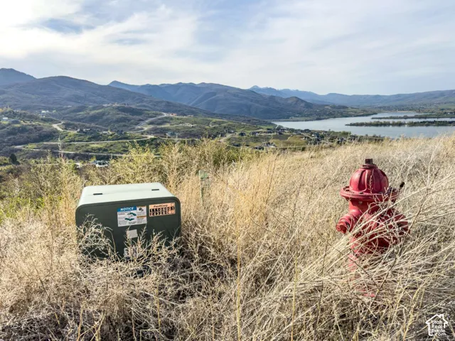 Expansive terrain featuring mountain scenery, a body of water, natural dry grasses, a fire hydrant, and utility equipment