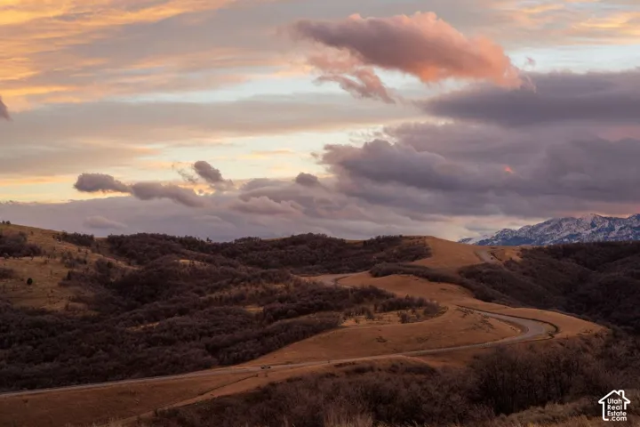 Expansive hilly terrain, rolling landscape, paved access road, and snow-capped mountain peaks under a sunset sky