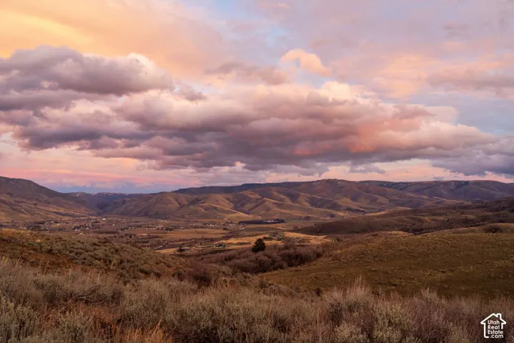 Expansive mountainous terrain featuring native brush, rolling hills, and a backdrop of atmospheric sunset clouds