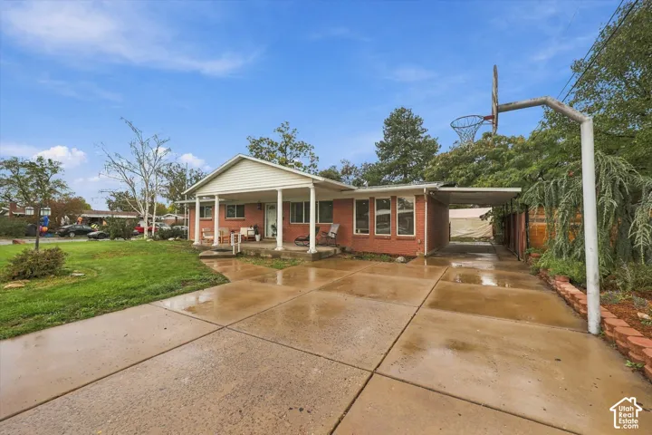 Single-story brick residence featuring a covered front porch, expansive concrete driveway, and integrated carport