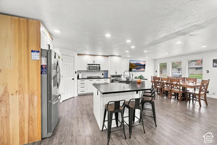 Kitchen featuring white cabinetry, dark countertops, a center island with bar seating, wood-finish flooring, and recessed ceiling lighting
