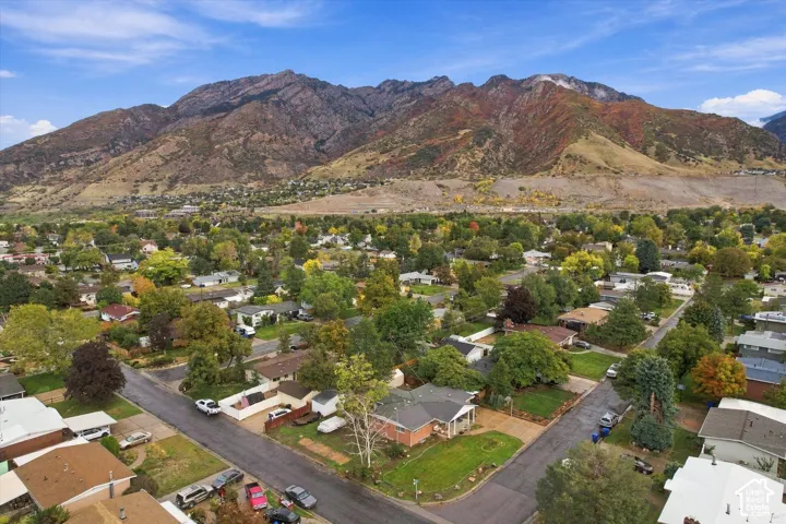 Aerial perspective featuring a brick-exterior residence situated on a corner lot with mature trees and a prominent mountain backdrop