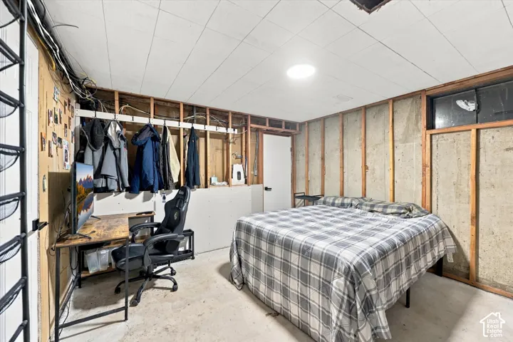 Unfinished room featuring exposed concrete walls, exposed wood wall studs, a drop ceiling, and a high-set slider window