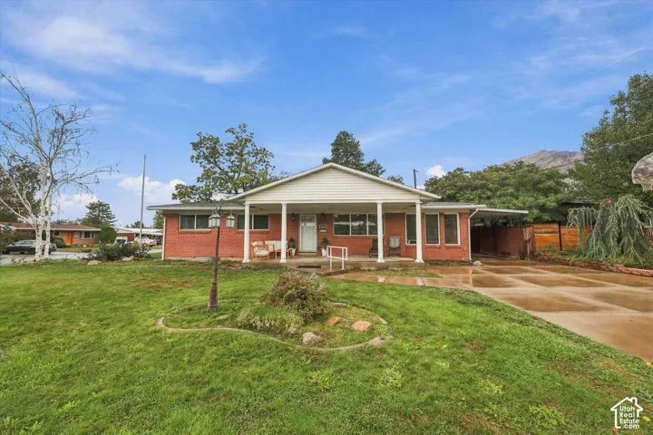 Single-story brick exterior featuring a covered front porch with columns, concrete driveway, and expansive front lawn