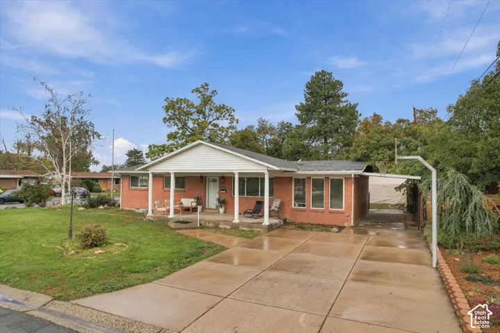 Brick exterior featuring a covered front porch, white support columns, multi-paned windows, and a concrete driveway with a carport