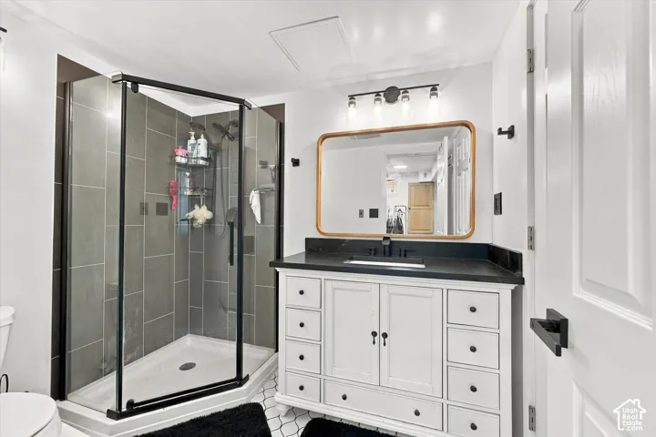 Bathroom featuring a walk-in shower with charcoal tile surround and black frame, white vanity cabinet with dark countertop, rectangular undermount sink, and three-light wall fixture