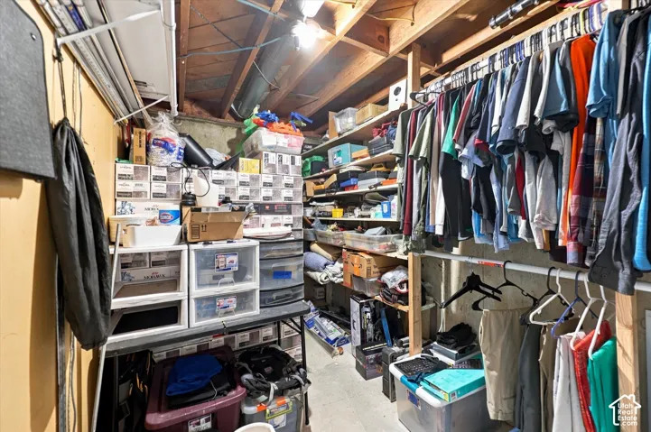Storage area featuring exposed ceiling joists, concrete walls, and built-in wood shelving