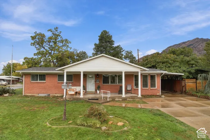 Single-story brick exterior featuring a covered front porch, concrete driveway, attached carport, and mountain backdrop