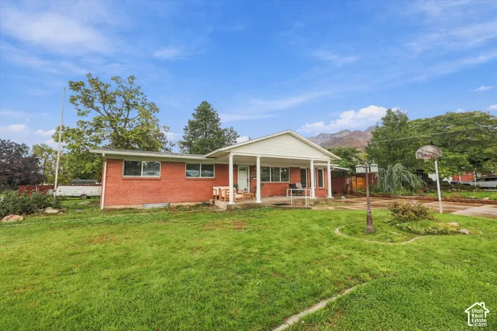 Exterior featuring red brick masonry, a covered porch with structural columns, expansive lawn, concrete hardscaping, and mountain backdrop