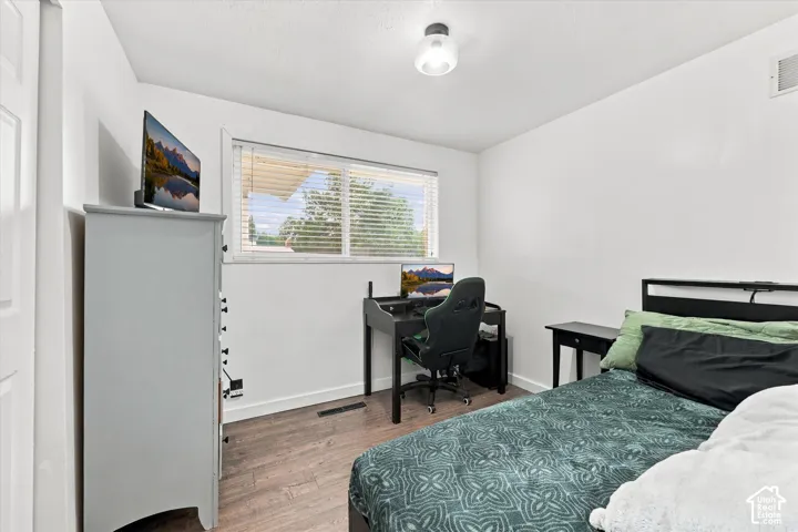 Bedroom featuring wood-finish flooring, a horizontal sliding window with horizontal blinds, and a circular flush-mount ceiling light fixture