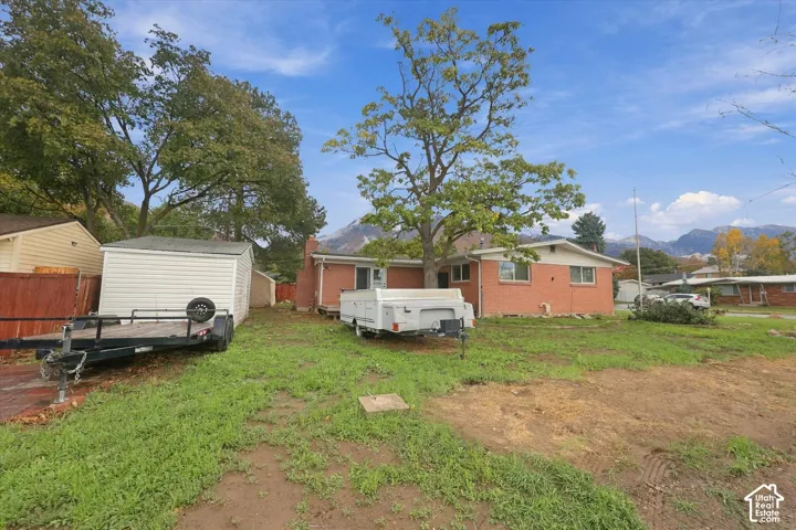 Single-story brick exterior featuring a detached storage structure, mature trees, and mountain backdrop