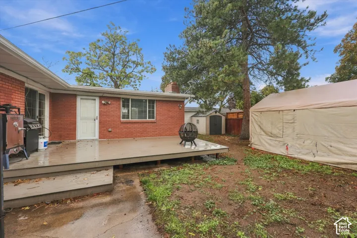 Red brick exterior featuring a raised deck, mature trees, and an additional storage shed